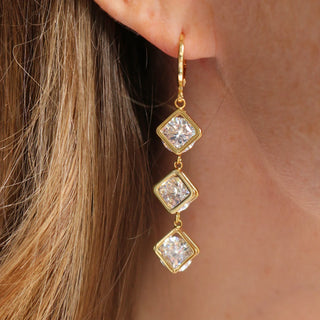 gold drop earring with three square-cut clear gemstones in gold settings.