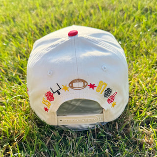 A cream-colored baseball cap with colorful embroidered football-themed designs and numbers