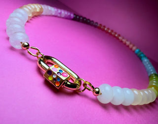 A beaded bracelet with translucent white beads, a gold-tone clasp decorated with colorful gemstones, and a multicolor gradient section of beads