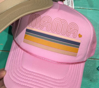 A pink trucker-style cap with 'MAMA' outlined across the front and horizontal stripes in beige, navy, yellow, and pink, with a small yellow heart. 