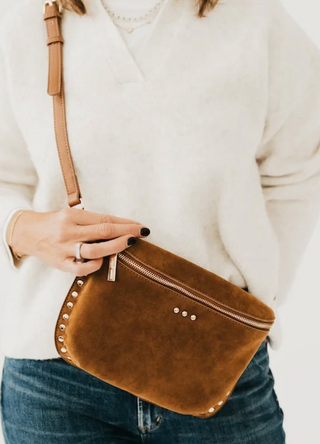 Brown leather crossbody bag held by a person wearing a white sweater and blue jeans.