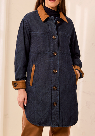 A woman wearing a quilted dark blue denim-style coat with tan collar, cuffs, and pocket trim