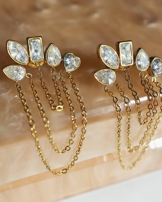 A pair of gold-toned statement earrings with clear marquise and rectangular gemstones and dangling chain elements