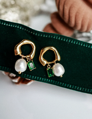 gold huggie hoop earrings with dangling white baroque pearls and small green square-cut stones