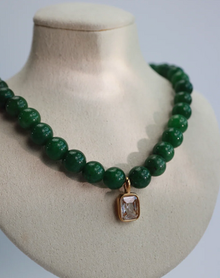 A green beaded necklace with a small gold rectangular pendant containing a clear faceted stone